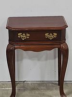 Front view of Queen Anne style table with closed drawer, showing cabriole legs with pad feet and brass hardware on drawer front.