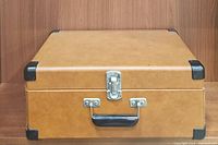 Closed view of the Crosley portable record player in tan wood case with black corner protectors and carry handle.