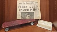 Vintage wooden skateboard with historic newspapers and pearl necklace in case beside it