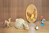 Photo shows entire set of six wooden animal and folk art figurines on a wooden surface against wood paneling background.
