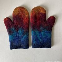 Top-down view of both felted wool oven mitts laid flat, showing front side with vibrant rust, red, blue, and navy colors.