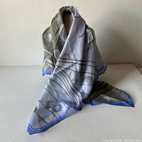 Silk scarf arranged upright showing overall pattern and colors of gunmetal grey and ultramarine blue on light background.