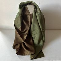 Silk scarf draped over a display, showing olive green and brown tones with hand-rolled edges.
