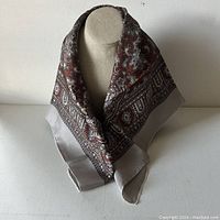 Square silk scarf displayed on a neutral fabric mannequin bust showing the overall paisley pattern and color scheme.