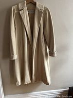 Full view of the vintage beige cashmere coat hanging showing front, lapel collar, and long sleeves.