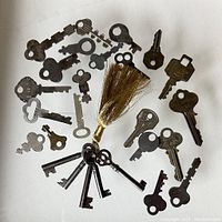 Overview of the collection showing skeleton keys attached to a gold-colored tassel and various loose old keys of different types and sizes.