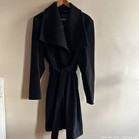 Full front view of the black wool coat showing its length, wide collar, and fabric belt.