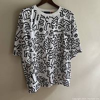 Front view of white Hugo Boss T-shirt with black Keith Haring inspired graphic art print hanging on wooden hanger.