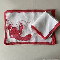 Placemats and napkins laid flat on a surface showing the lobster applique and red border detail.