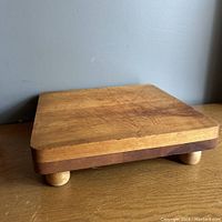 Angled side view showing thickness and rounded corners of the footed maple cutting board with wear marks.