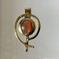 Front view of the modernist brass pendant showing circular brass frame and reddish-brown glass cabochon.