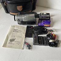 Overview of camcorder with accessories including batteries, tapes, remote, cables, connectors, manual and case