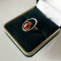 Front angled view of modernist sterling silver ring with oval amber in gift box.