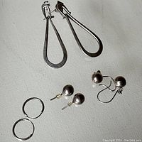 Photo showing all earrings in the lot arranged on a white surface: two hinged teardrop earrings, two small silver ball stud earrings, two dangling ball earrings, and two small hoops.
