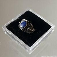 Top angle view of the sterling silver Navajo ring with blue stone and leaf design on black base inside transparent display box.