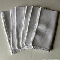 Photo of six white linen napkins folded and stacked, showing overall size and condition.