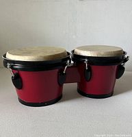 Side view of Westbury bongo drums showing red wooden bodies with black rims and natural drum heads.