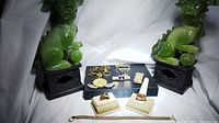 Full lot of 14k gold filled and gold plated collectible jewelry and accessories displayed on black and cream holders, surrounded by green Foo Dog statues
