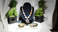 Photo of semi precious stone necklace displayed with green Foo Dog statues and three bracelets spread out beneath the necklace.
