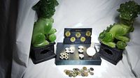 Full lot displayed with all items centered including collectible coins, button covers, watch, and bracelet with coin charms, flanked by decorative foo dog statues.