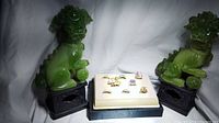 Photo showing eight assorted rings placed on a cream jewelry display with two green Foo Dog statues on either side.