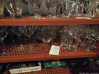 Two shelves filled with assorted clear glasses including various wine, beer, margarita, and water glasses plus some low ball glasses on a perforated metal shelf.