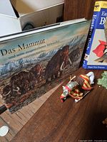 Photo of books including 'Das Mammut' in German, horse with rider figurine on wooden surface