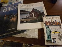 Over Europe, Maine, New York coffee table books arranged on dark wooden surface.