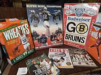 Image showing Wheaties cereal box featuring Larry Bird, New England Patriots Super Bowl Champions poster, Budweiser Boston Bruins poster, and various sports memorabilia including magazines and DVD cases.