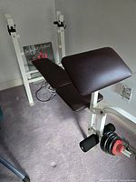 Full view of the exercise bench showing brown padded seat and backrest with white metal frame and leg lift attachment