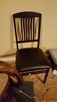 Side view of folding chair with curved vertical wooden slats on backrest and black cushioned seat indoors.