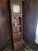 Full view of grandmother sized wooden clock with glass door, Roman numeral clock face, and open shelves below