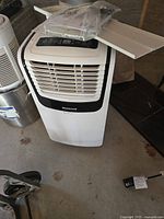 Front view of white and black Honeywell portable air conditioner with control panel and window kit parts on top.
