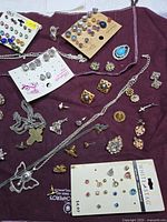 Overhead photo of multiple jewelry items spread on maroon cloth showing earrings, necklaces, and pendants.