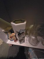 Shelf with assortment of vases including Mikasa hexagonal vase with landscape painting, ceramic floral vase, pink bud vase, and clear glass vases.