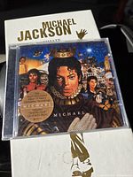 Michael Jackson The Ultimate Collection CD cover with artwork showing Michael Jackson with crown and collage background, white box partially visible beneath.