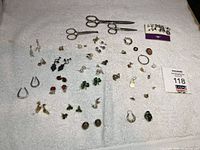 Photo showing various earrings arranged on a white towel including multiple matching pairs, along with two vintage metal scissors on the upper side of the layout.