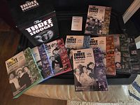 Photo of the full boxed set including all 20 DVDs fanned out in front of the box on a black surface.