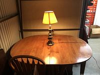 Oval wooden dining table assembled with a lamp and chair on it, showing the glossy wood surface and oval shape.