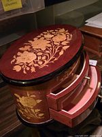 Closed oval wooden jewelry box with floral inlay on lid and sides, showing two drawers pulled out