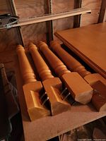 Four turned wooden legs with metal brackets leaning against a plywood wall next to the tabletop.