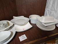 White dishes and serveware including plates, platters, butter dish, and jello mold arranged on a wooden surface.