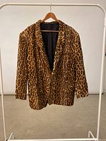 Full view of the leopard print blazer hanging on a wooden hanger on a white clothing rack, showing front and shape.