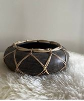Side view of the black clay pot showing the rattan lattice weaving around its rounded body, placed on a white furry surface.
