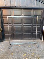 Full front view of the assembled chrome garment rack standing upright in front of garage door with castors visible on base.
