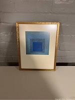 Framed print showing the full artwork with wood frame against a brick wall background.