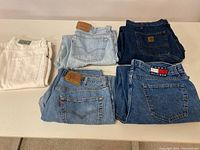 Top view of five folded jeans showing labels including Levi's, Carhartt, Tommy Hilfiger, and others