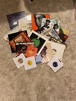 Full view of loose vinyl records including 45s, 12" singles, and LP albums laid out on carpet.