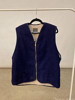 Front view of navy blue corduroy vest on black hanger showing full zipper closure and V-neck.