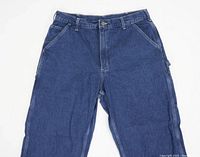 Front view of blue denim Carhartt carpenter jeans laid flat showing pockets, zipper fly, and belt loops.